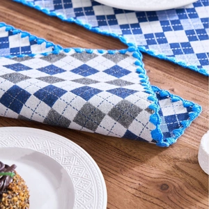 Blue and white plaid fabric placemat with decorative crochet pom-pom edges on a wooden table