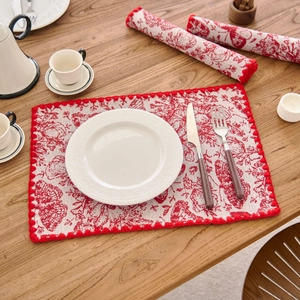 Macro shot of rectangular red jacquard floral placemat with pom-pom trim on wood table