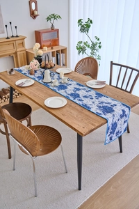 Detail of floral table runner with blue patterns on white fabric over a wooden table