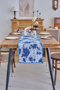 Detail of navy floral table runner with elegant blue pom pom trim on a wooden table