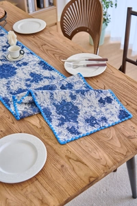 Close-up of blue and white floral table runner with decorative blue pom-pom trim and texture