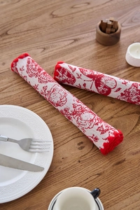 Detailed view of red floral and butterfly embroidered placemats rolled on a wooden table