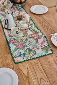 Close-up of jacquard table runner with tropical monstera leaves and embroidered lace edges