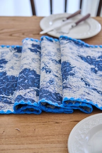 Detail of blue floral jacquard table runner with decorative lace borders on a wooden table