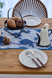 Macro shot of navy floral jacquard table runner with blue pom-pom fringe on a wooden table