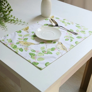 Detail of linen table mat with yellow bird and green leaf print on a white table