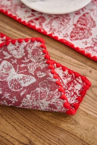 Close-up of jacquard butterfly embroidery and red pom-pom fringe on fabric placemat