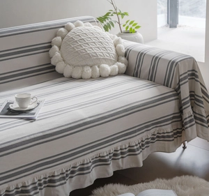 Detail of striped sofa cover with pleated hem and a white knitted round pom-pom pillow