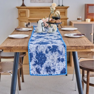 Navy blue jacquard table runner with white floral patterns and blue pom-pom fringe trim