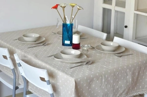Detailed view of beige cotton linen tablecloth with white daisy prints and lace edging
