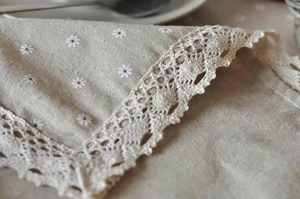 Detail of embroidered daisy pattern and crochet lace edge on linen tablecloth