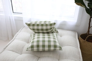Detail of green and white gingham pillow covers on a soft white tufted ottoman