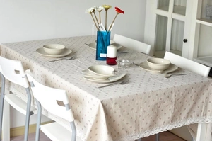 Close-up of beige linen tablecloth with small dots and white lace trim in a rustic style