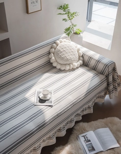 Close-up of minimalist striped cotton sofa cover with ruffled edges and pompom pillow