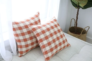 Detail of two orange and white plaid cotton linen pillow covers on a gray textured sofa