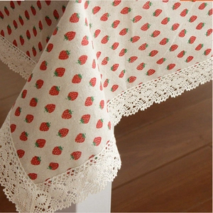 Close-up of beige cotton linen tablecloth with red strawberry print and lace trim