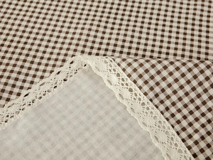 Detail of brown gingham tablecloth with white lace trim and cotton linen texture