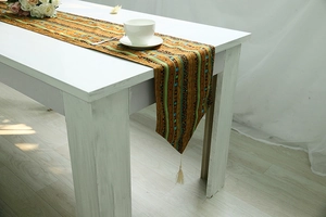 Ethnic style table runner with colorful stripes and beige tassel on wooden table