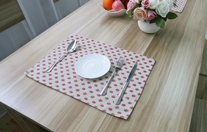 Detail of strawberry print cotton linen table mat on a rustic wooden dining table