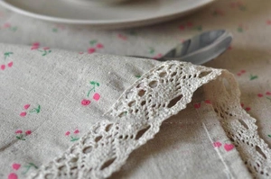 Close-up of pink cherry print cotton linen fabric with intricate beige crochet lace trim