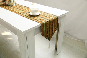 Detail of bohemian mustard yellow table runner with ethnic patterns and beige tassels