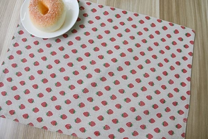 Close-up of cotton linen table mat with red strawberry patterns on a wooden table