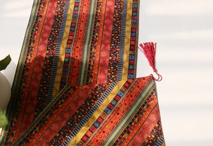 Detailed shot of ethnic jacquard table runner with bohemian patterns and red silk tassels