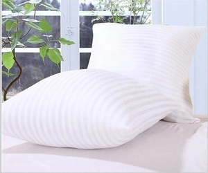 Detailed view of two white striped pillows with fluffy PP cotton filling on a bed
