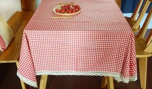Detail of red gingham cotton linen tablecloth with white lace edges on a wooden table