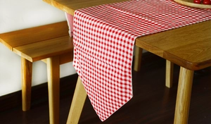 Detail of red gingham cotton linen table runner on a wooden dining table