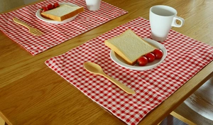 Detail of red and white checkered linen placemats set on a rustic wooden dining table