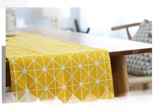 Detail of yellow cotton linen table runner with white geometric grid on dark wood table