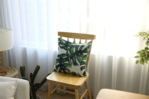 Detail view of square pillow case with tropical monstera leaf print in a cozy home setting