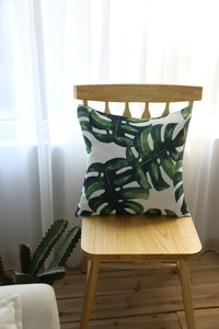 Close-up of Monstera leaf print on a square linen cushion placed on a wooden chair
