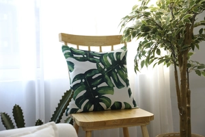 Detail view of tropical Monstera leaf pattern pillow case on a wooden chair in a sunlit room