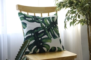 Detail of tropical monstera leaf print on square cushion cover placed on wooden chair