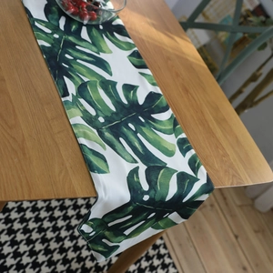 Tropical monstera leaf table runner on light wood dining table in a cozy home setting