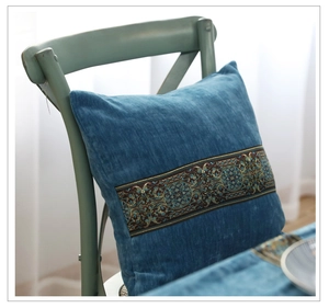 Detailaufnahme vom blauen Samtkissen mit Stickerei auf einem Holzstuhl im Zimmer