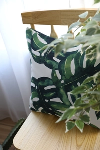 Macro shot of Monstera leaf print pillow on a wooden chair with light curtains