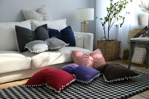 Detail of bow-shaped decorative pillows with pom-pom edges in various solid colors
