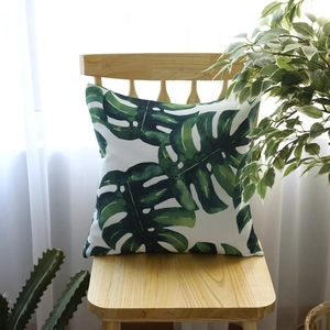 Square monstera leaf print pillow cover on wooden chair with white curtain background