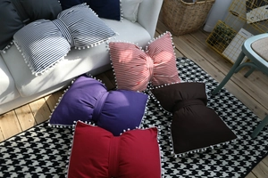 Detail of bow-shaped decorative pillows with pom-pom trim on a cozy white sofa