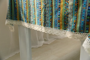 Close-up of bohemian multi-color striped cotton linen tablecloth with white lace trim