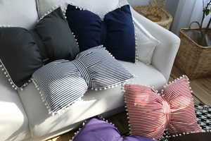 Detail of bow-shaped pillows with white pom-poms in various colors and striped patterns
