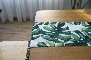 Detail of Nordic table runner featuring green monstera leaf print on white cotton fabric