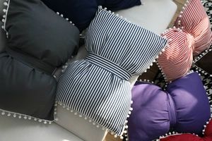 Detailed view of striped and solid bow-shaped throw pillows with pom-poms on a sofa