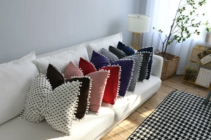 Detail of Nordic striped and solid pillows with pom-pom edges on a white sofa