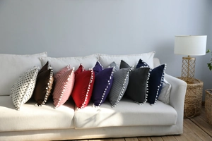 Close-up of decorative poms on colorful striped and solid pillows on a white sofa