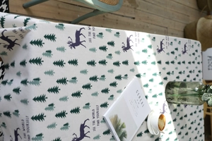Close-up of linen tablecloth featuring green pine trees and deer motifs with text