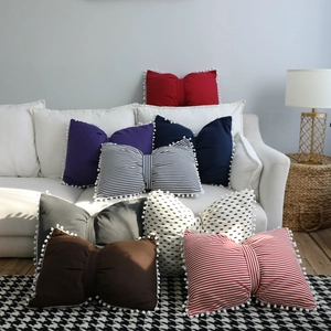 Detail of creative bow-shaped cushion with pom-pom trim on a stylish fabric sofa